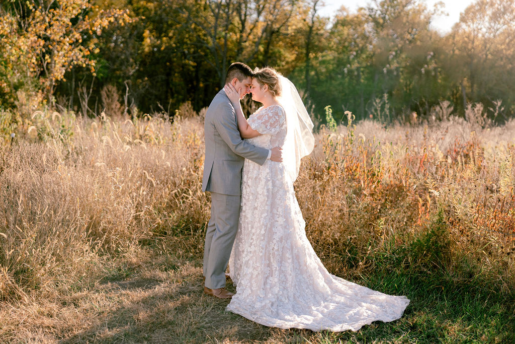 Bride and groom embrace forehead to forehead in a wild grass field during sunset at Wild Rye KC Ranch